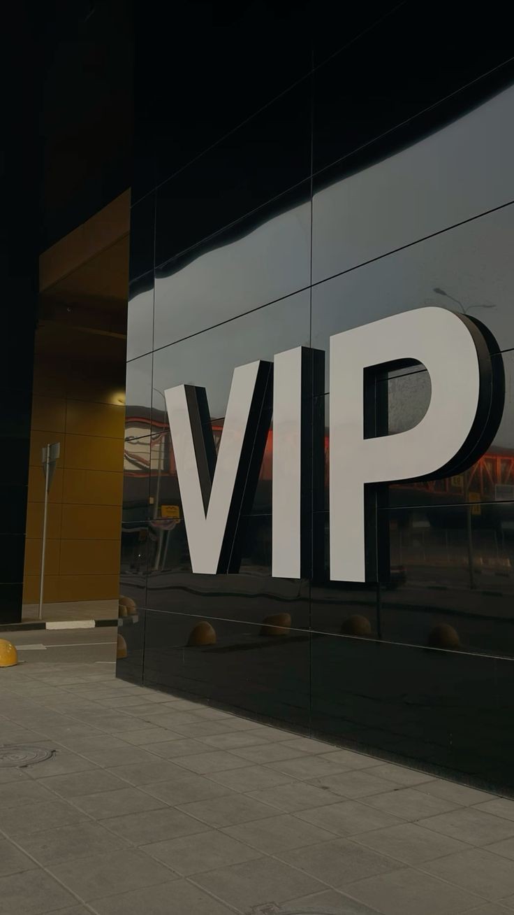 Large white 'VIP' sign on a dark reflective wall outside a building with sidewalk visible.