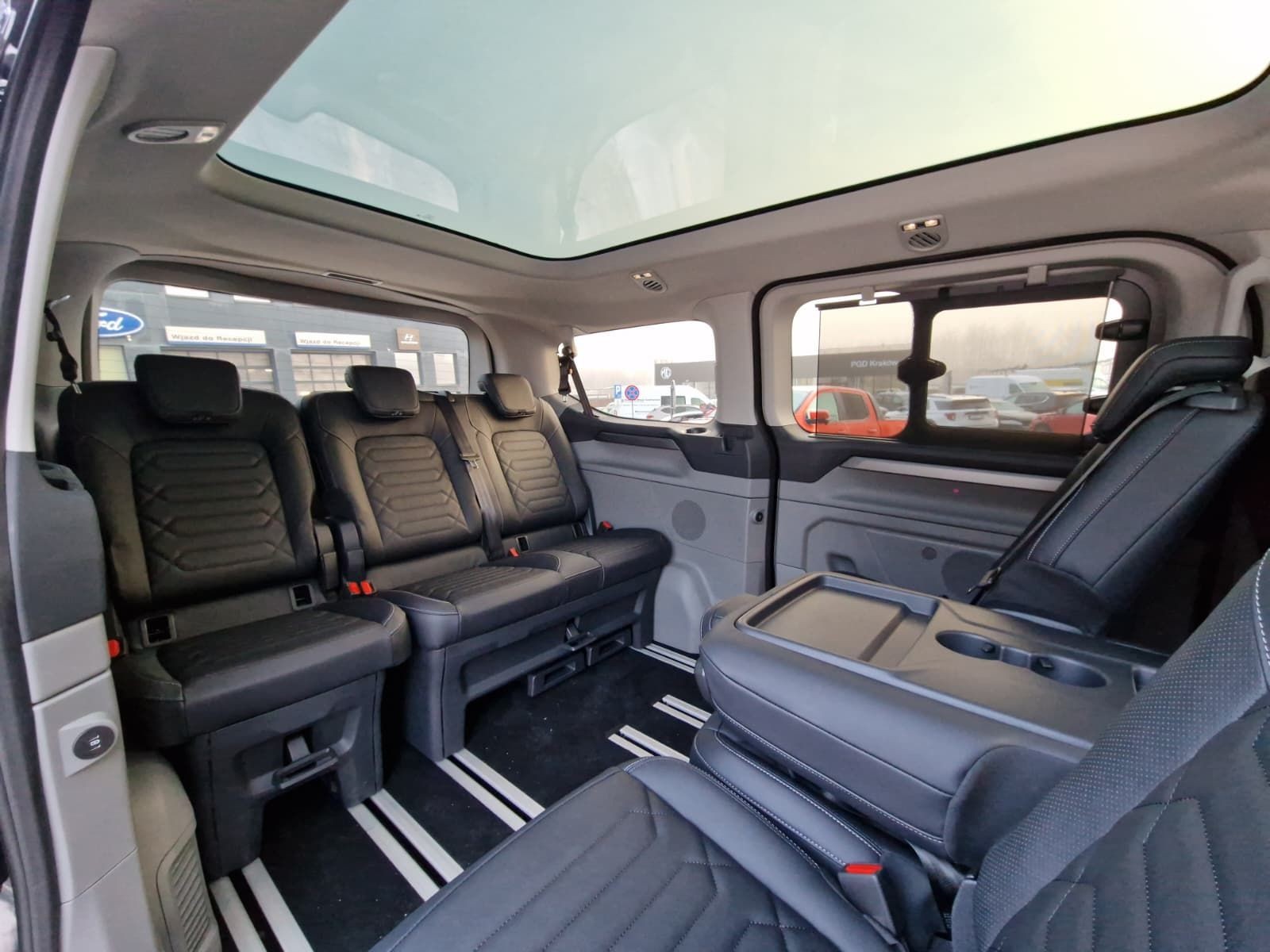 Interior of a vehicle with multiple rows of black leather seats and a panoramic sunroof.
