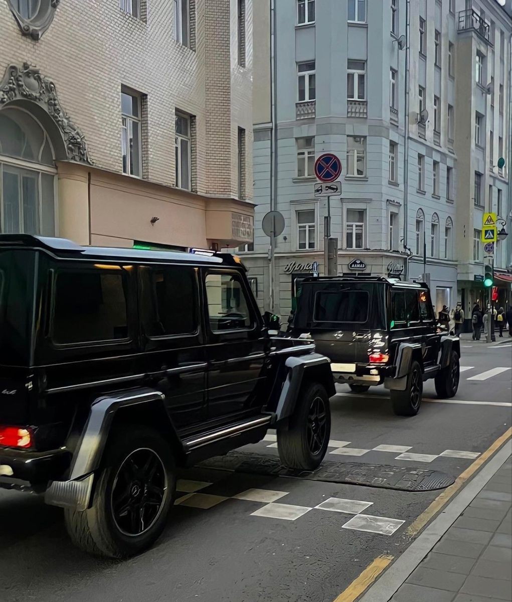 Two black SUVs driving through an urban street lined with ornate and modern buildings.